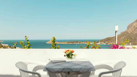 Utsikt över havet från en balkong med ett bord, två stolar och en vas med blommor. (AI-genererad text)