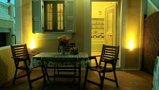 En terrass med ett bord och två stolar, belyst under kvällstid, med en öppning mot ett interiör. (AI-genererad text)