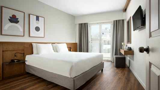 Modernt hotellrum med dubbelsäng, konst på väggen och balkong med glasdörr. (AI-genererad text)