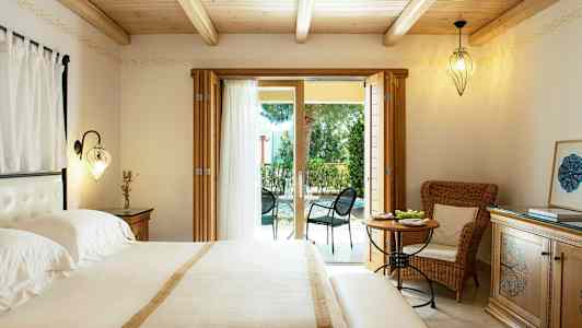 Ett sovrum med dubbelsäng, ljusa möbler och glasdörrar som leder till en möblerad uteplats. (AI-genererad text)