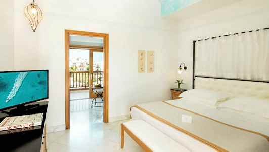 Interiör av ett hotellrum med en säng, en TV, och en öppning till en balkong. (AI-genererad text)