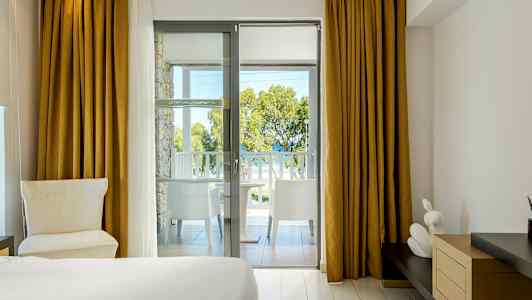 Hotellrum med utsikt från balkong mot träd och hav. (AI-genererad text)