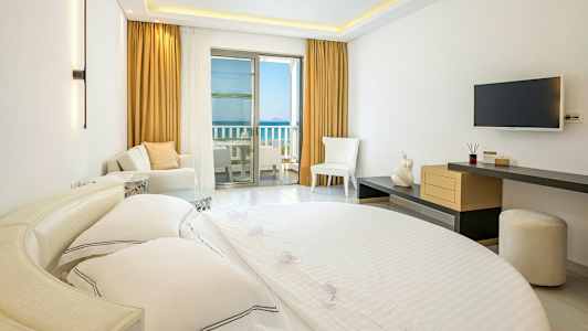 Interiör av ett hotellrum med en säng, sittmöbler och en balkong med havsutsikt. (AI-genererad text)