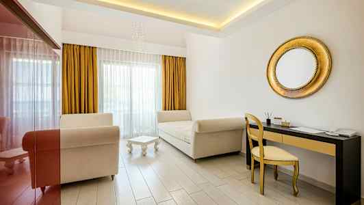 Bild på ett ljust rum med två soffor, ett litet bord, guldfärgad spegel och skrivbord med stol. (AI-genererad text)