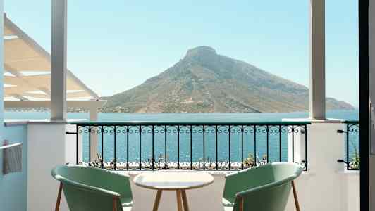 Två stolar och ett bord på en balkong med utsikt över havet och ett berg. (AI-genererad text)