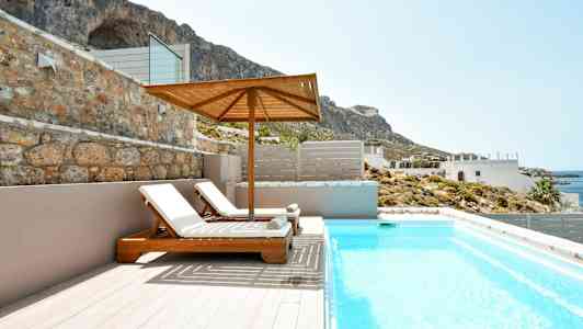 Två solstolar under ett parasoll vid en pool med utsikt mot kusten och berg. (AI-genererad text)