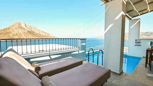 Två solstolar vid en liten pool med havet och bergslandskap i bakgrunden. (AI-genererad text)