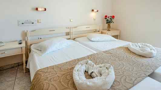 Ett hotellrum med två enkelsängar, prydnadsföremål och en vas med blommor på ett nattduksbord. (AI-genererad text)