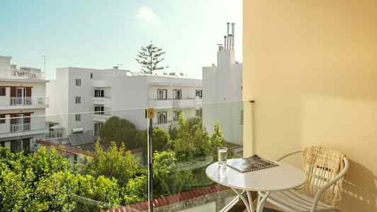 Balkong med bord och stol, utsikt över vita byggnader och grönska. (AI-genererad text)