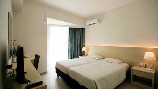 Hotellrum med två enkelsängar, skrivbord med tv och lampa på nattduksbordet. (AI-genererad text)