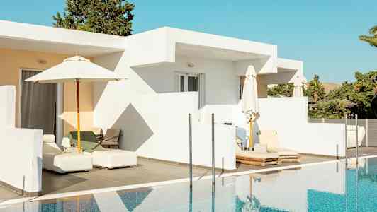 En vit byggnad med uteplats och solstolar vid en pool. (AI-genererad text)