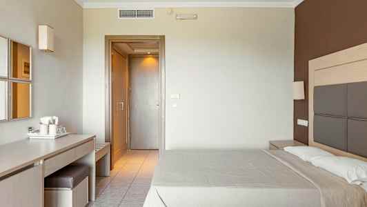 Hotellrum med en dubbelsäng, ett skrivbord med stol och spegel, samt en dörr till övriga utrymmen. (AI-genererad text)