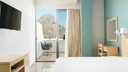 Hotellrum med en säng, skrivbord och balkong med utsikt över ett berg. (AI-genererad text)