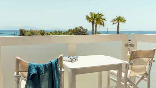 Utblick från en balkong med bord och stolar samt havsutsikt i bakgrunden. (AI-genererad text)