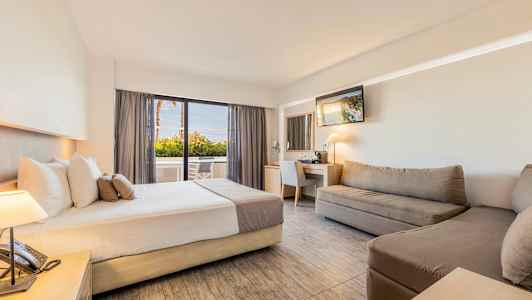 Ett hotellrum med en säng, soffor, arbetsbord med spegel, och en sittgrupp nära ett glasfönster. (AI-genererad text)