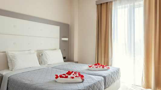 Ett hotellrum med två enkelsängar som är dekorerade med röda rosenblad. (AI-genererad text)