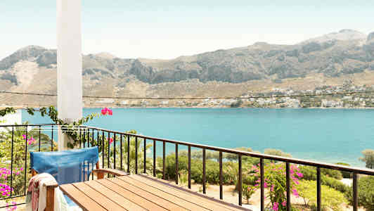 En balkong med bord och stol med utsikt över havet och berg i bakgrunden. (AI-genererad text)