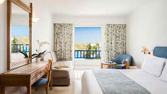 Ett hotellrum med balkong, möbler inklusive säng, skrivbord, stol och fåtölj. (AI-genererad text)