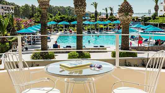 En balkon med ett glasbord och stolar, med utsikt över en pool med solstolar och palmer. (AI-genererad text)