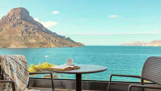 Ett bord med en kopp och bok står på en balkong med utsikt över havet och ett berg. (AI-genererad text)