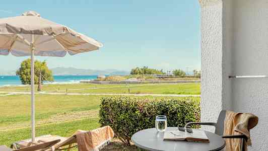 Utsikt från terrass med bord, stolar, parasoll och grönområde mot havet. (AI-genererad text)
