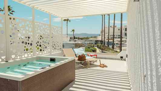En terrass med jacuzzi, solstolar och utsikt mot palmer och byggnader i bakgrunden. (AI-genererad text)