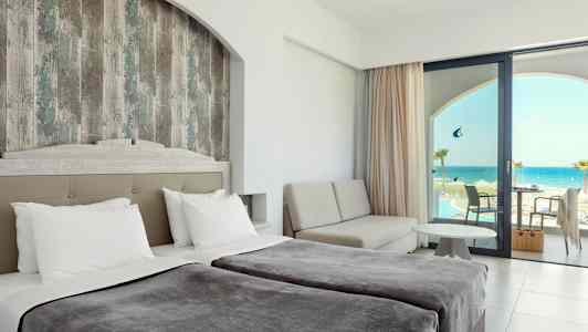 Hotellrum med dubbelsängar, en sittgrupp och utsikt över havet genom en glasdörr. (AI-genererad text)