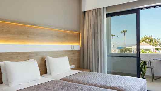 Hotellrum med två enkelsängar och utsikt mot en uteplats och hav i bakgrunden. (AI-genererad text)