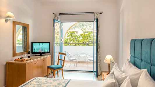 Ett hotellrum med en säng, en byrå med en TV och en balkong med stolar och bord. (AI-genererad text)