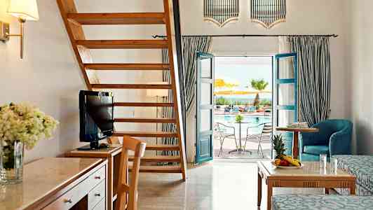 Ett rymligt hotellrum med trämöbler, en trätrappa, och en dörr som leder ut till en pool. (AI-genererad text)