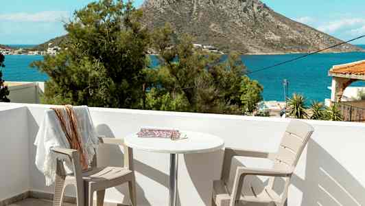 Utsikt från en uteplats med två stolar och ett bord, mot havet och en klippa i bakgrunden. (AI-genererad text)