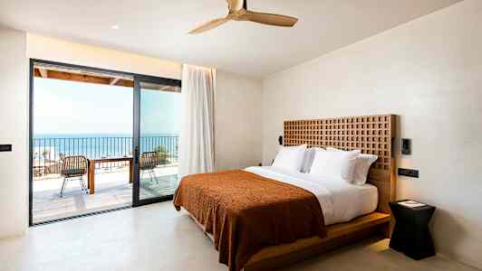 Hotellrum med dubbelsäng och utgång till en balkong med havsutsikt. (AI-genererad text)