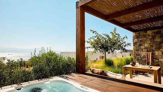 Bild av en terrass med ett spabad och trädgårdsmöbler, havet synligt i bakgrunden. (AI-genererad text)