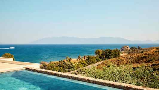 Utsikt över en pool, kusten och havet med en båt som passerar. Bergen syns i bakgrunden. (AI-genererad text)