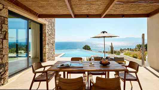 Utomhus veranda med träbord och stolar, utsikt över pool och hav. (AI-genererad text)