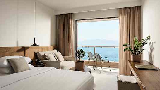 Ett hotellrum med en säng, soffa och utsikt över havet från en balkong. (AI-genererad text)