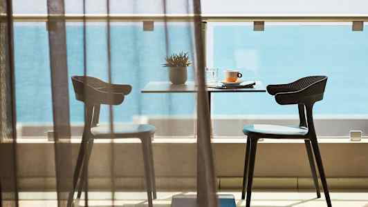 En bord med två stolar på en balkong framför havsutsikt. (AI-genererad text)