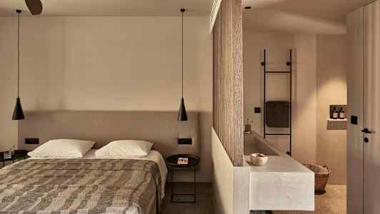 Ett sovrum med en dubbelsäng, en avdelare som separerar ett badrum med diskho och handdukshållare. (AI-genererad text)