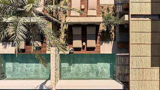 Vy uppifrån av solstolar och två pooler, med en palm bredvid. (AI-genererad text)