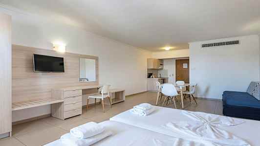 Ett hotellrum med säng, skrivbord, TV och matplats med köksutrustning. (AI-genererad text)