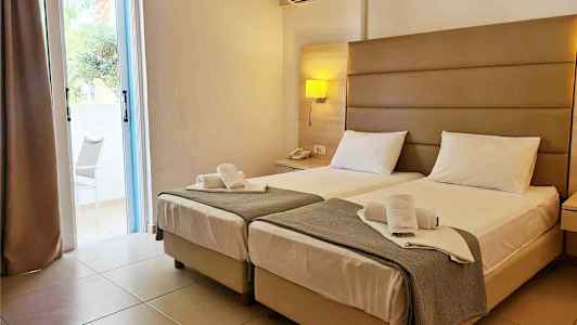 Hotellrum med två enkelsängar, nattduksbord och en luftkonditionering på väggen. (AI-genererad text)