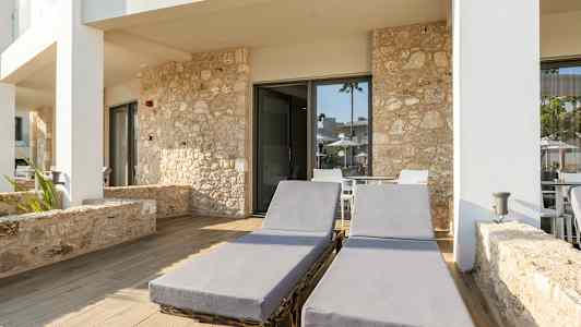 Två solstolar på en stenlagd uteplats framför byggnad med stenfasad. (AI-genererad text)