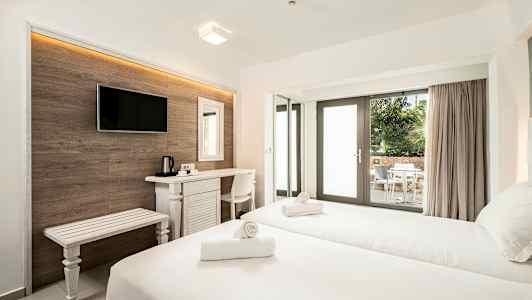 Ett hotellrum med två sängar, skrivbord, TV och en uteplats med bord och stolar synlig genom glasdörrar. (AI-genererad text)