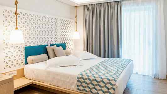 Hotellrum med en dubbel säng, stilren inredning och ljusa gardiner. (AI-genererad text)