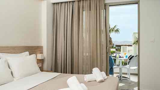 Hotellrum med bäddad säng och handdukar placerade ovanpå, med en balkongdörr som vetter mot en terrass. (AI-genererad text)