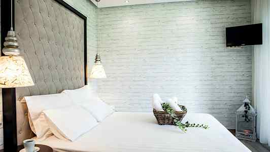 Ett rum med en säng, vita sängkläder och en korg med handdukar och gröna växter. (AI-genererad text)