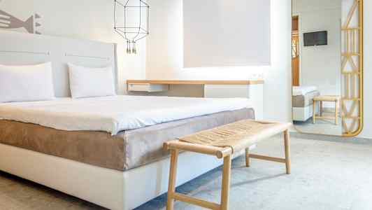 Ett modernt hotellrum med dubbelsäng, sittbänk och väggspegel. (AI-genererad text)