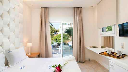 Hotellrum med vit säng, dekorationer och utsikt mot en grönskande terrass genom stora fönster. (AI-genererad text)