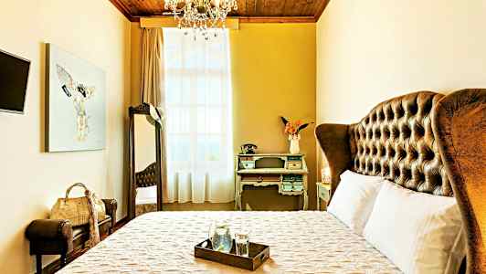 Ett elegant hotellrum med en stor säng, vintage skrivbord och dekorativ taklampa. (AI-genererad text)