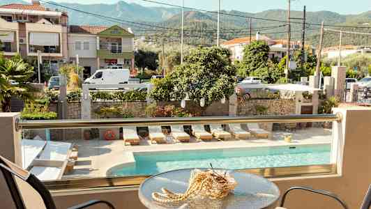 Utsikt från en balkong med bord och stolar mot en pool, solstolar och omgivande byggnader. (AI-genererad text)